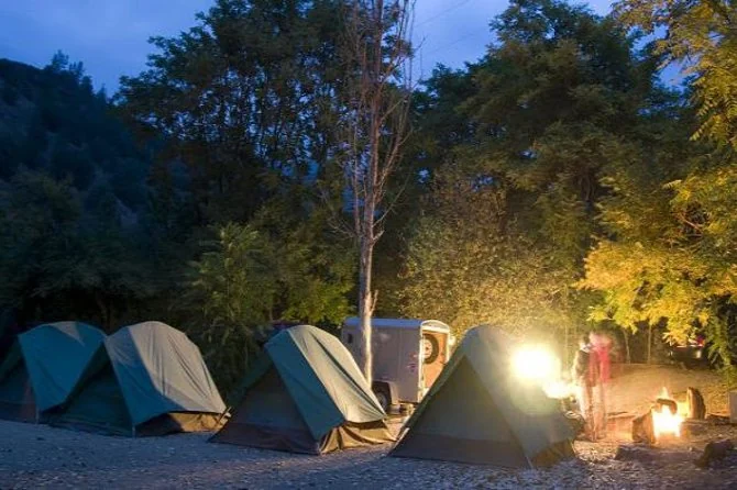 Tiendas verdes en un camping arbolado al anochecer, con un farol encendido